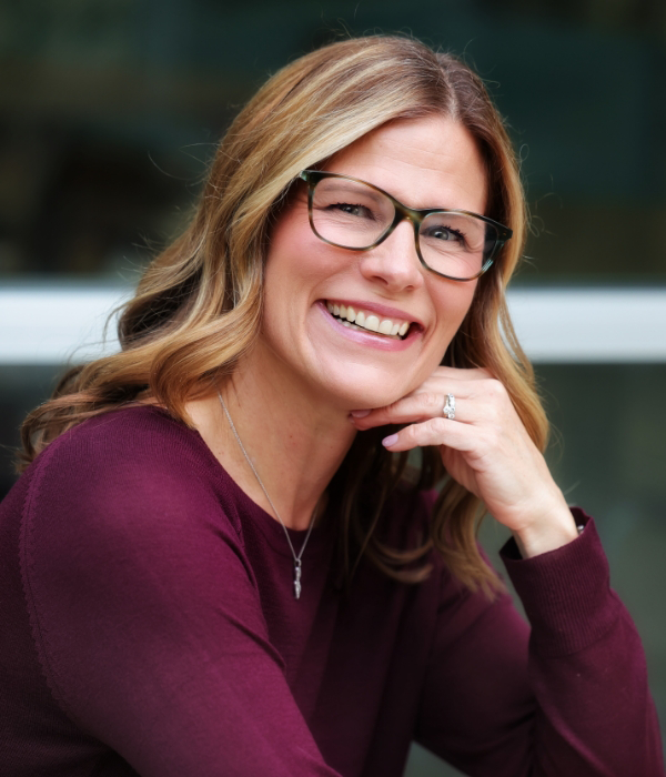Ashley Ward smiles with glasses and a maroon top.