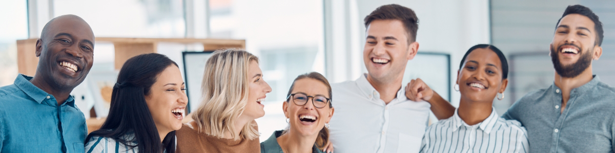 Group of seven diverse people standing close together indoors, all smiling and laughing.