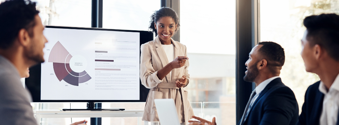 A woman presents a pie chart on a screen to four colleagues in a meeting room.